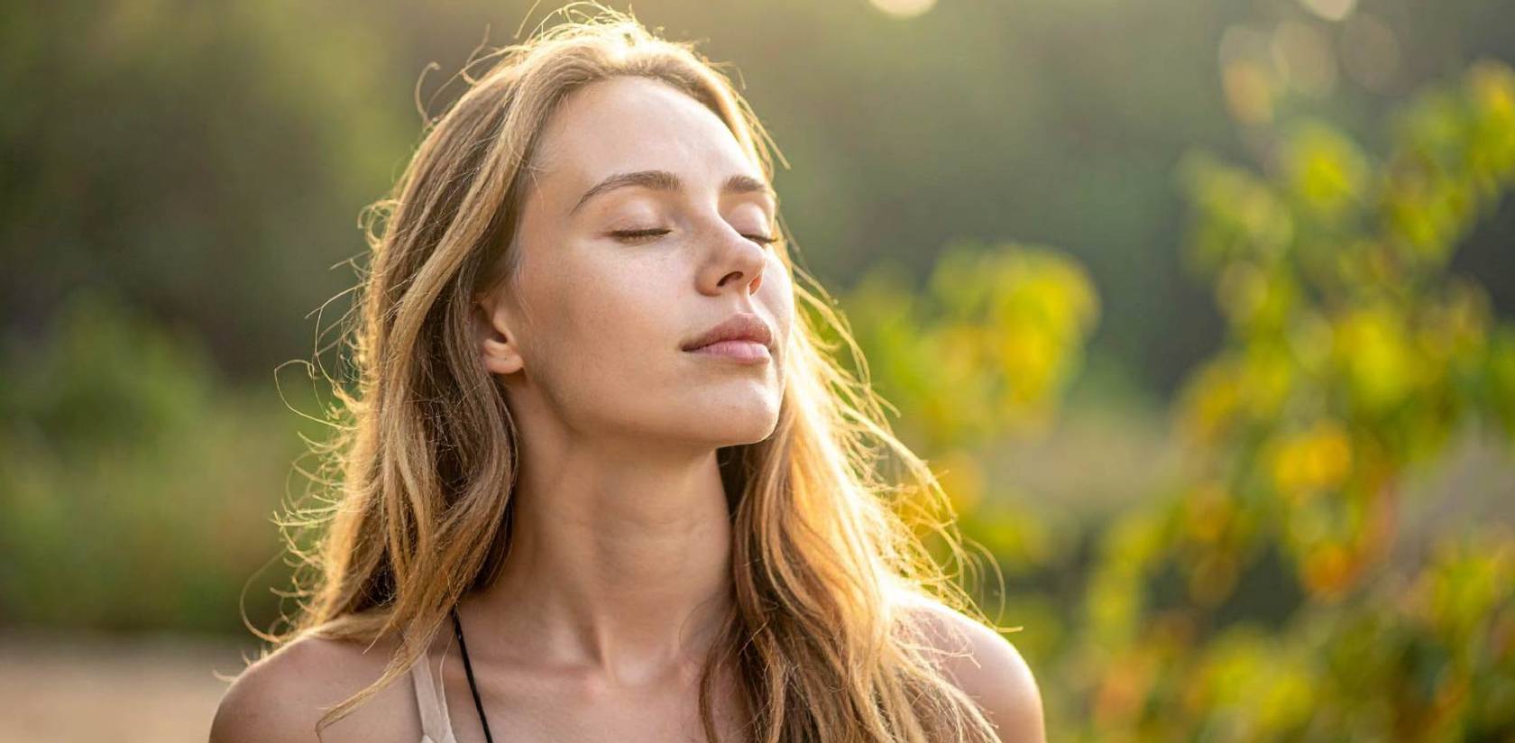 Woman with eyes closed outdoors, appearing relaxed and refreshed. Image represents wellness, self-care, recovery, stress relief, and overall well-being, often associated with LED light therapy and healthy lifestyle routines.