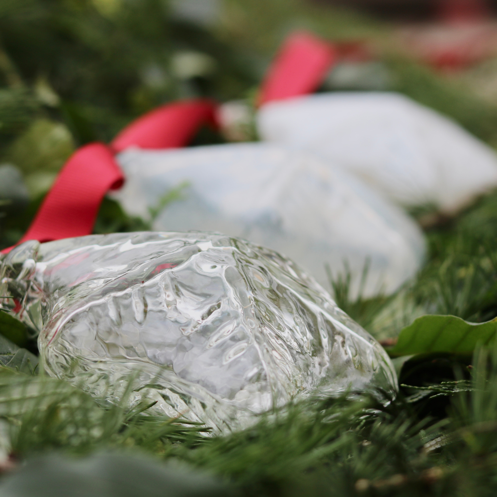 Three Snowflake ornaments with a red ribbon on a bed of greenery. 