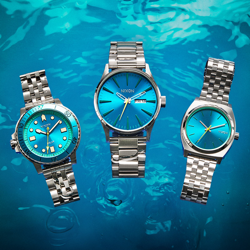 All three Stainless Steel and Teal Blue watches of the Nixon watches in the Aquatic Collection, featured in water. 