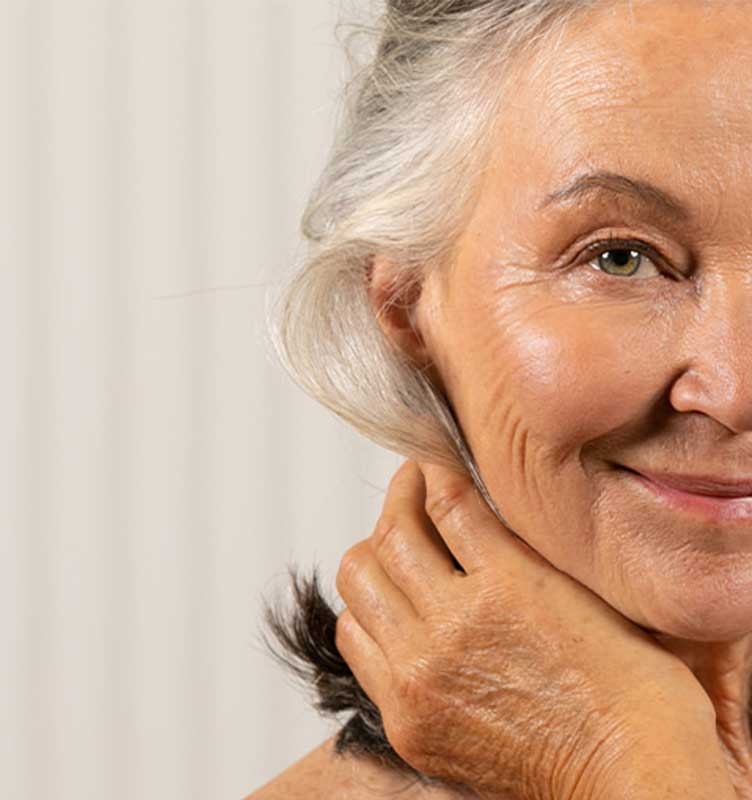 Older woman smiling at camera while she holds hair out of her face