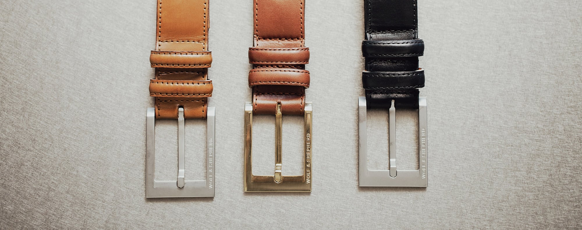 3 belts laid side by side, focusing on the buckle for Black, Honey, and Maple