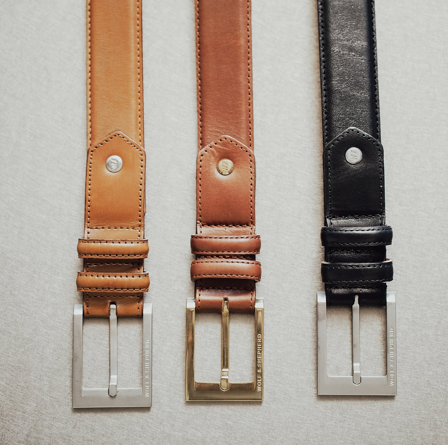3 belts laid side by side, focusing on the buckle for Black, Honey, and Maple