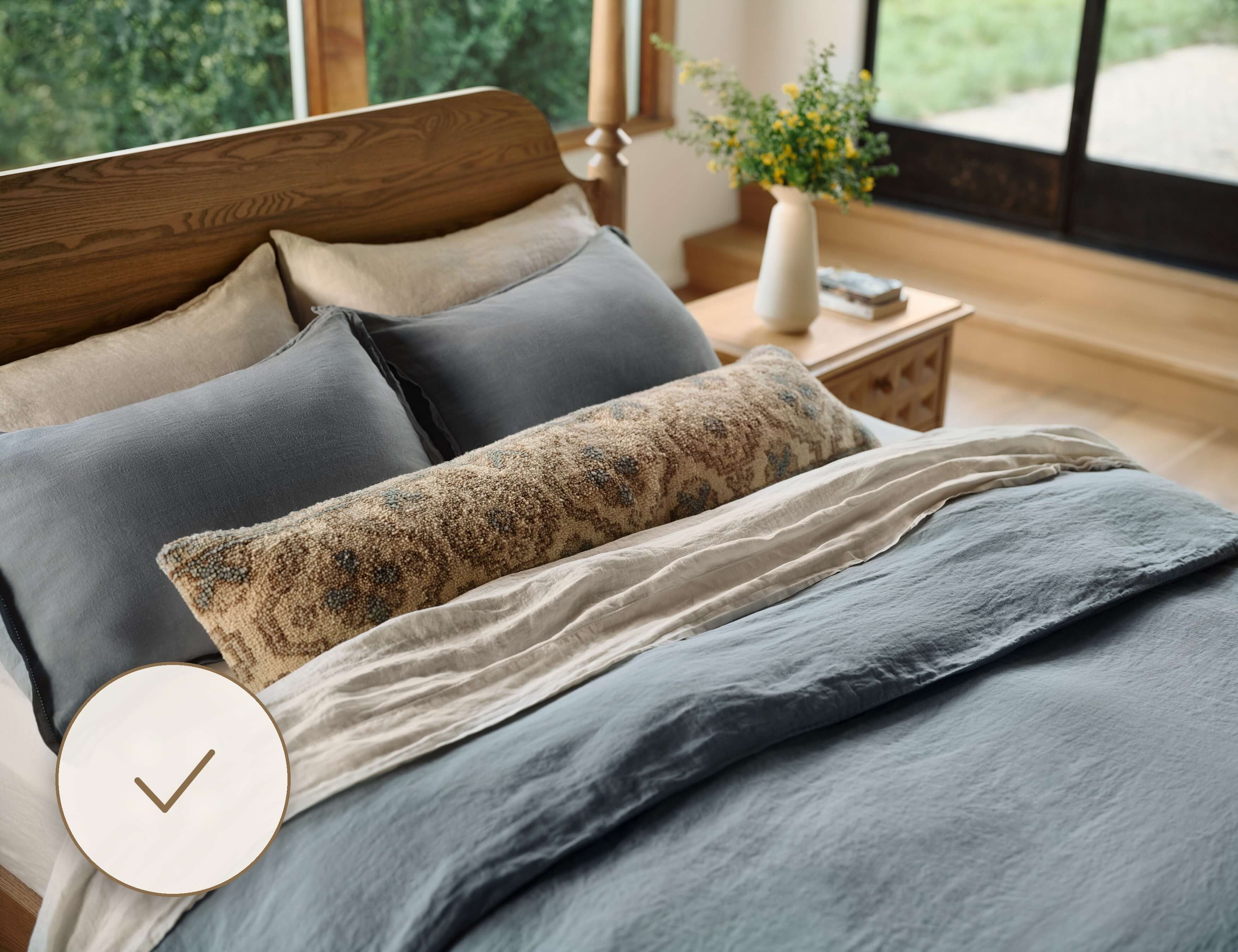 Wood bed frame with layered neutral and patterned bedding in a bedroom setting