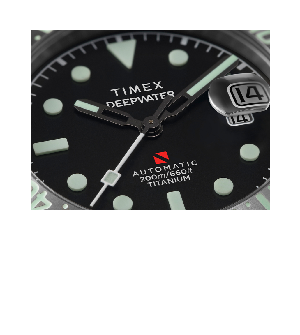 Detail shot of the Timex Deepwater watch’s dial showing the luminous markers, hands, and the automatic depth rating “200m/660ft TITANIUM” along with the red diver-down symbol. The magnifying cyclops lens over the date is prominently featured.