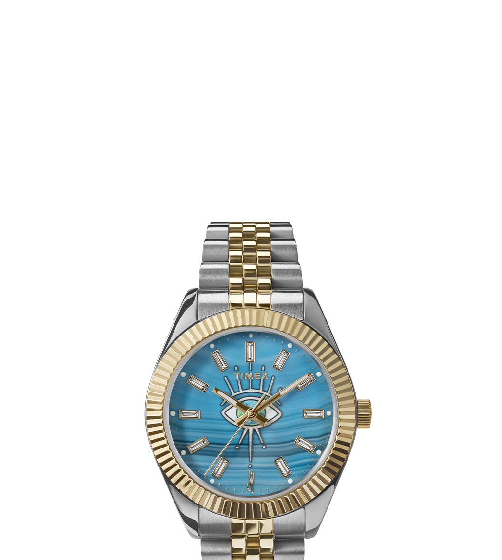 Front-facing view of the Timex x Jacquie Aiche watch on a white background. The watch showcases a turquoise dial with an eye motif, crystal hour markers, gold-tone hands, and a silver and gold two-tone bracelet with a fluted gold bezel.