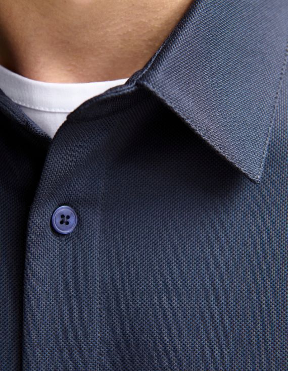 Close-up of a navy textured button-up shirt collar, with a white undershirt visible and a blue button detail.