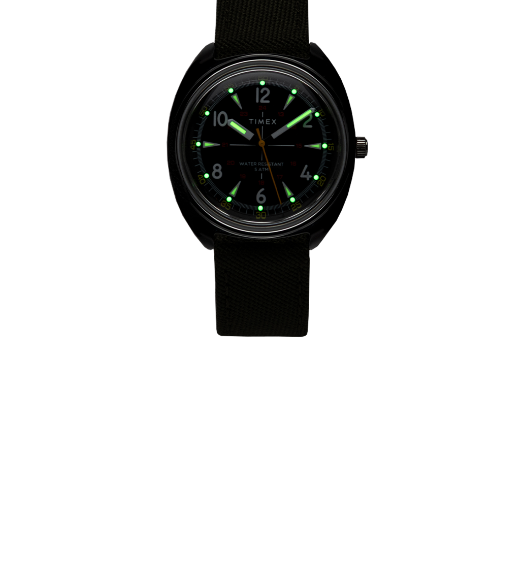 Timex x Bespoke Post watch in a dark setting with glowing green luminous hour markers and hands, highlighting its nighttime visibility.