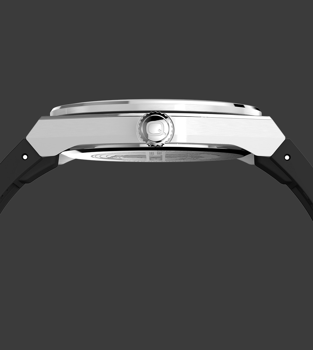 Side profile of the Q Timex® Continental GMT watch showing the slim brushed stainless steel case, ridged crown engraved with the ‘Q’ logo, and black synthetic strap.