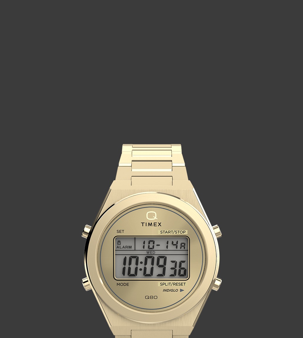 Front view of the Q Timex® Q80 Continental digital watch in gold-tone stainless steel, featuring a round case, digital display with day, date, and time, and four functional buttons on the bezel.