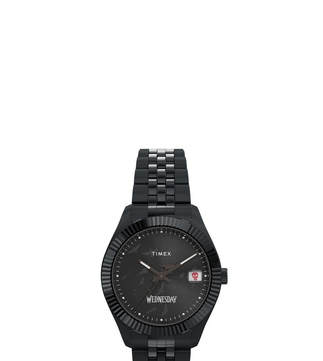 Front-facing view of the Timex x Wednesday Legacy watch, showcasing a black case, black dial with raven details, a red skull icon in the date window, and the “Wednesday” logo at the 6 o’clock position, paired with a polished black link bracelet.
