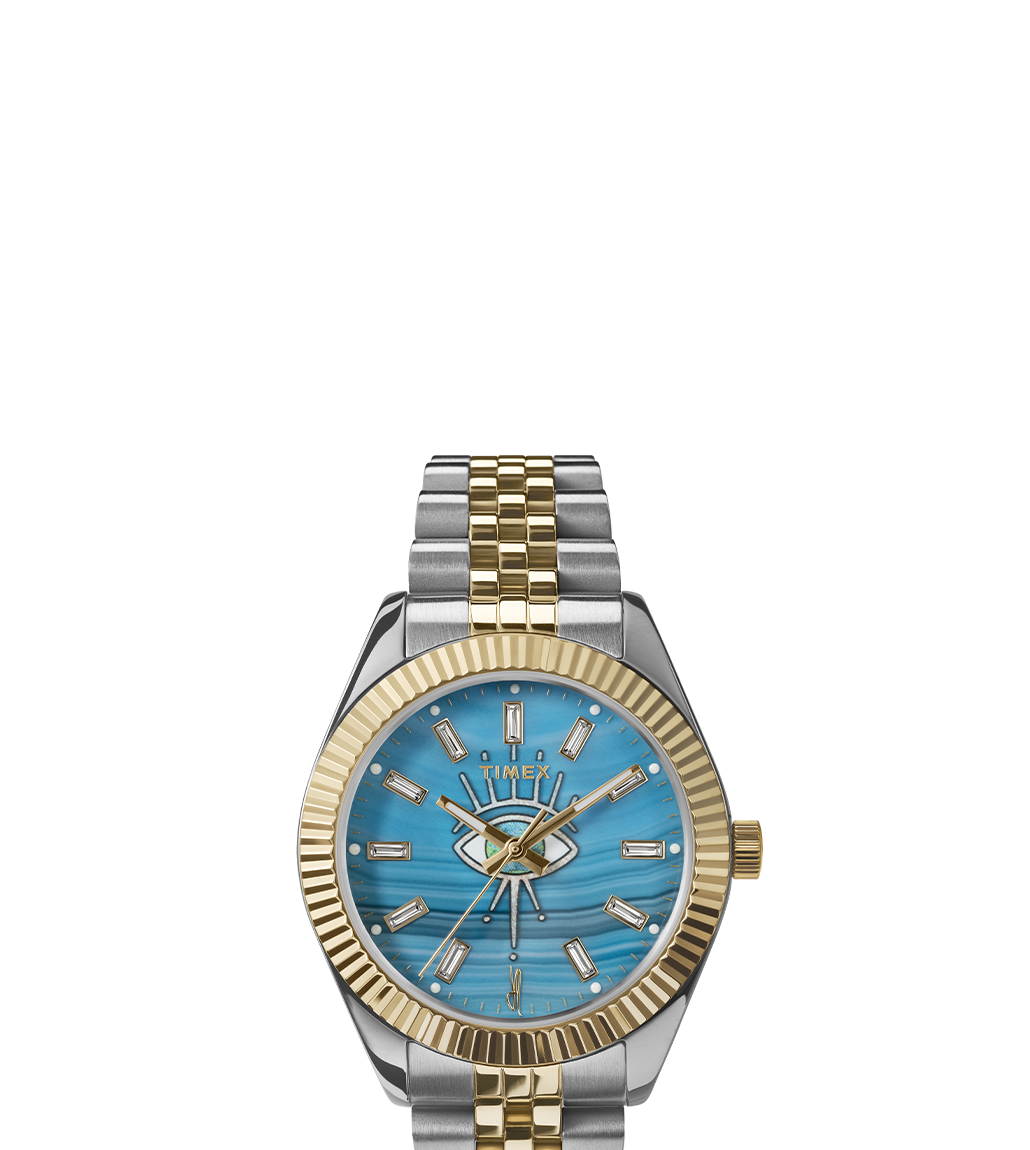 Front-facing view of the Timex x Jacquie Aiche watch on a white background. The watch showcases a turquoise dial with an eye motif, crystal hour markers, gold-tone hands, and a silver and gold two-tone bracelet with a fluted gold bezel.