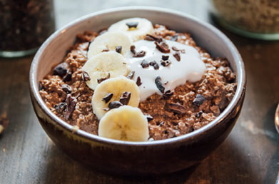 Bowl of oatmeal made with Navitas Essential Blend Cacao & Greens topped with bananas and fresh ingredients
