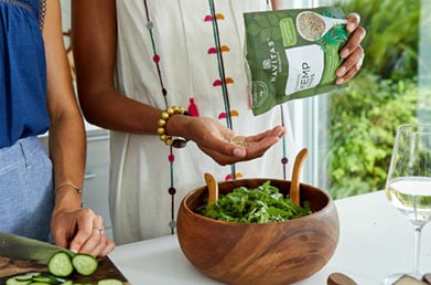 Sprinkling Navitas Hemp Seeds from the package onto a bowl of freshly-made salad