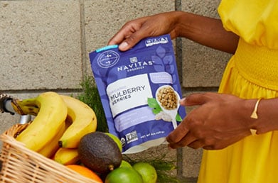 Person placing package of Navitas Mulberries into basket of fresh fruit