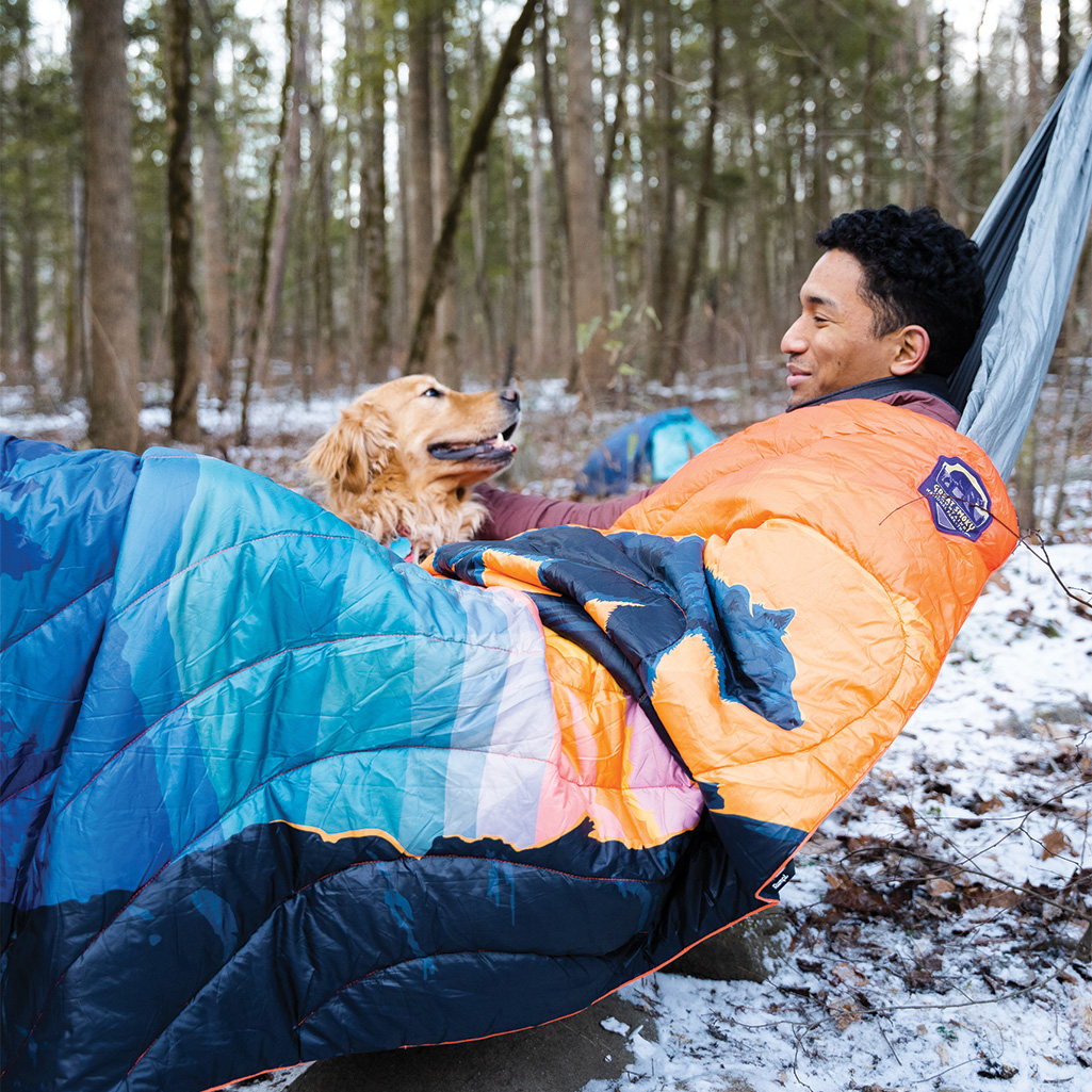 A man and his dog relaxing on a hammock outdoors with a Rumpl National Parks Blanket