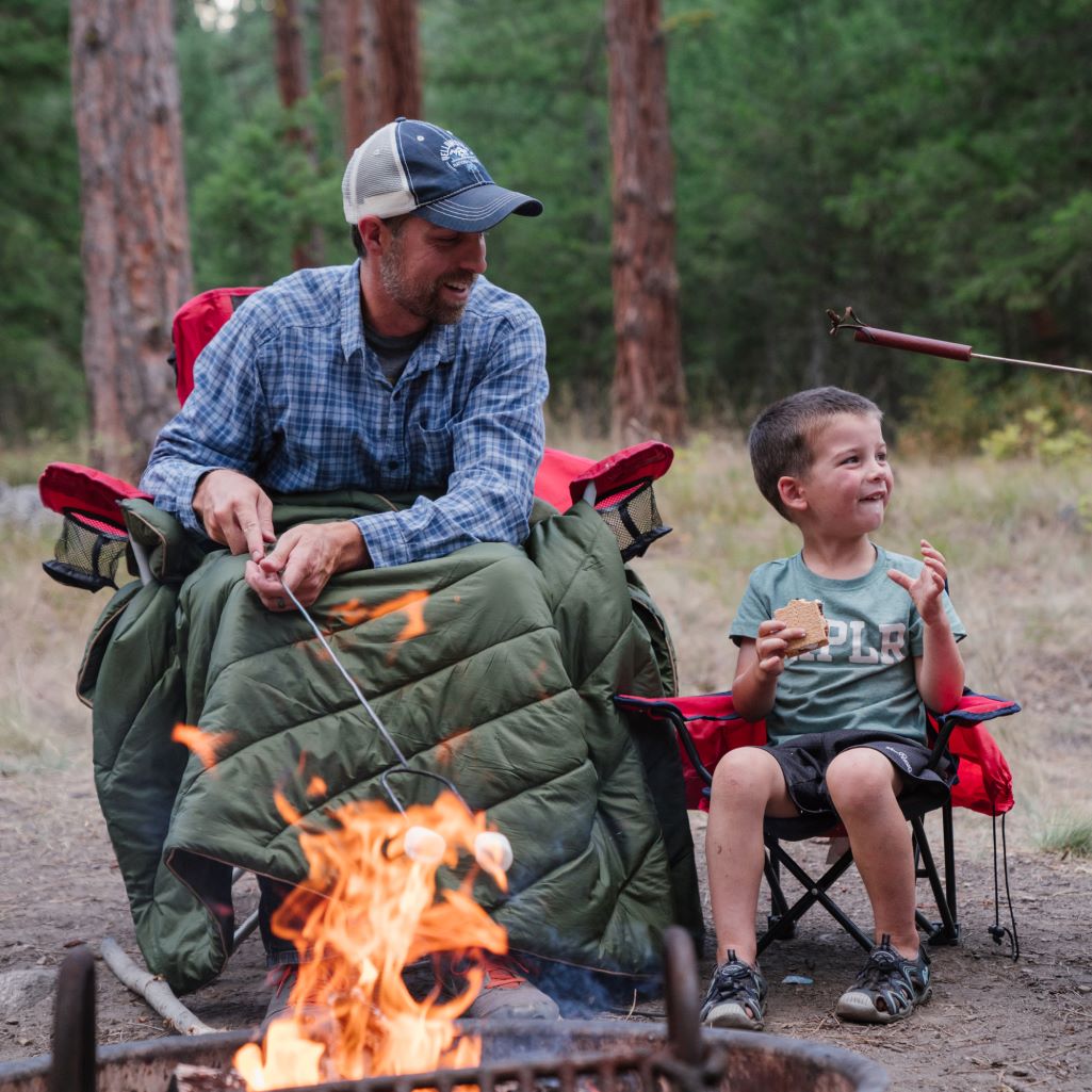 A father and sun share a snack and a Rumpl blanket by the campfire.