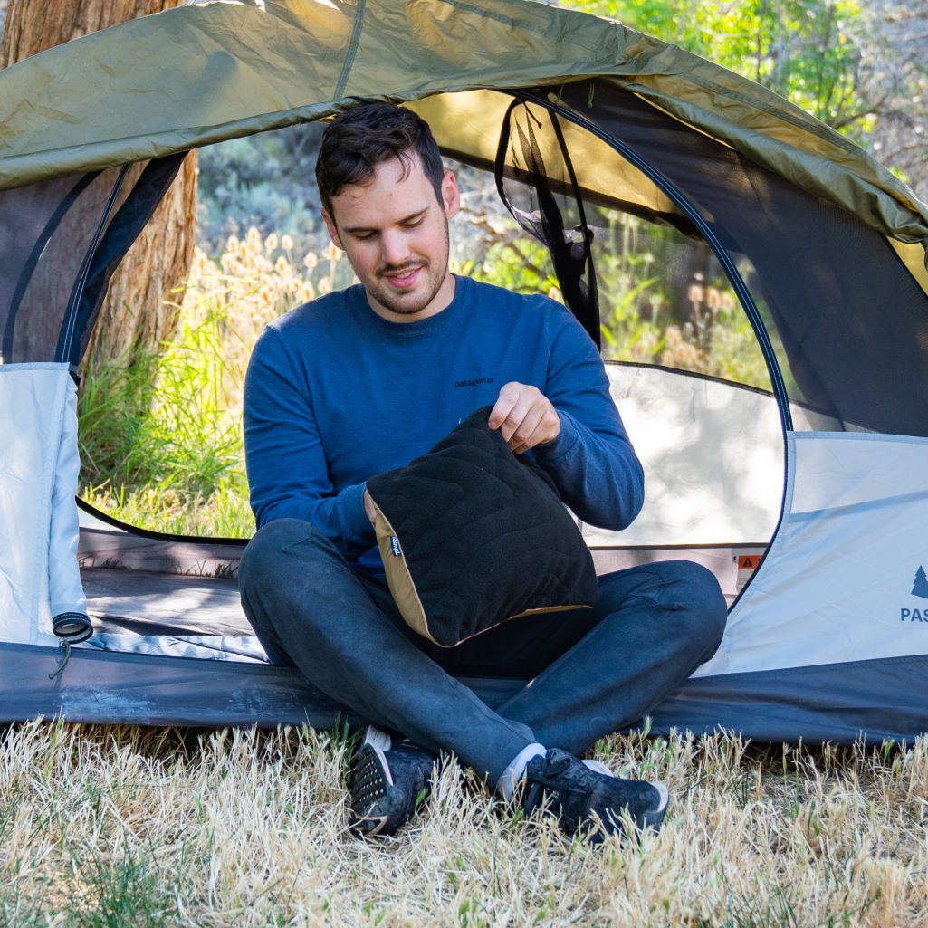 A man stuffs his jacket into a Rumpl Stuffable Pillowcase for an instant camp pillow.