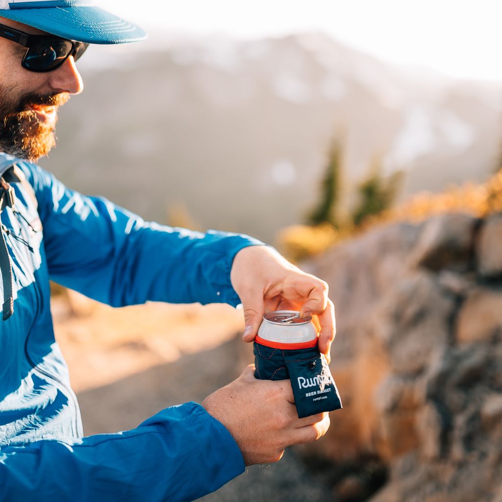 A man opens his can of beer, using a Rumpl Beer Blanket beer cozy to keep his hands warm and his drink cold.