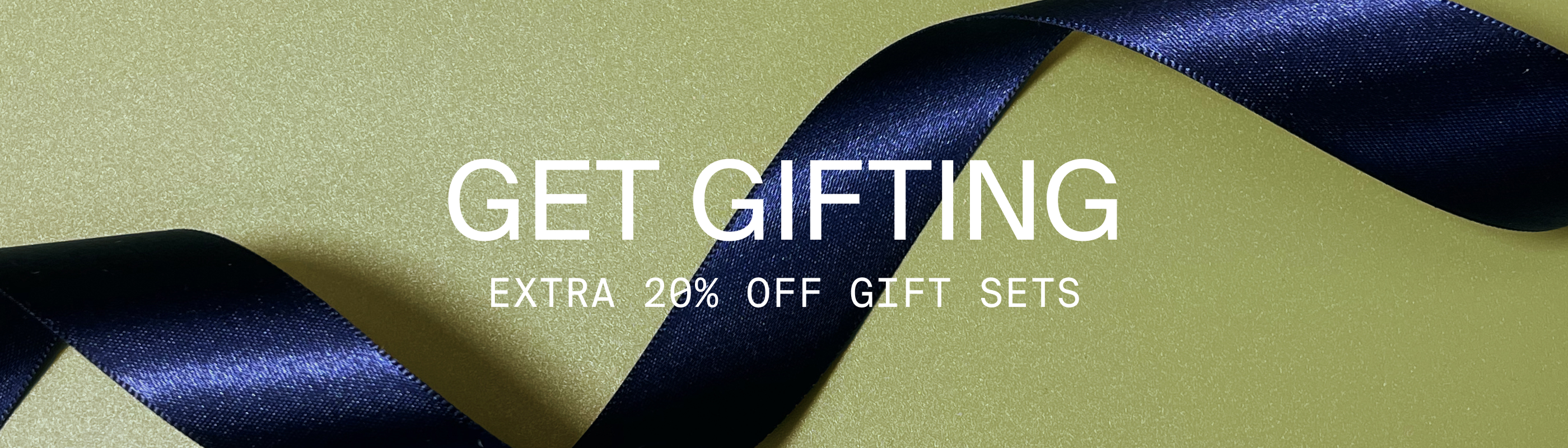 Image of a blue ribbon on a green background. Get gifting. Extra 20% off gift sets.