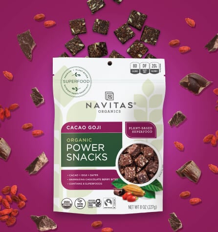 A package of Navitas Organics Cacao Goji Power Snacks against a purple background surrounded by chocolate bites and goji berries.
