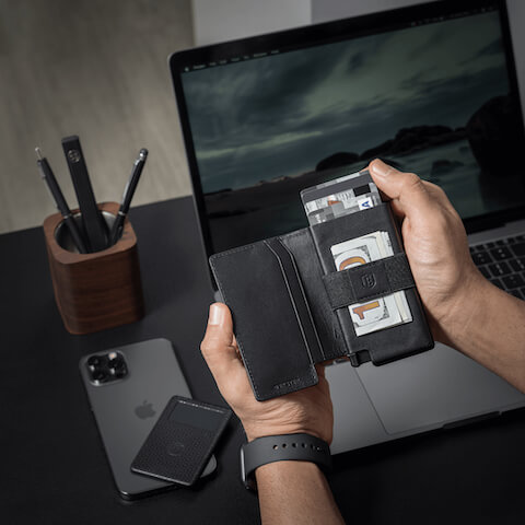 person holding leather smart wallet with other smart devices in the background