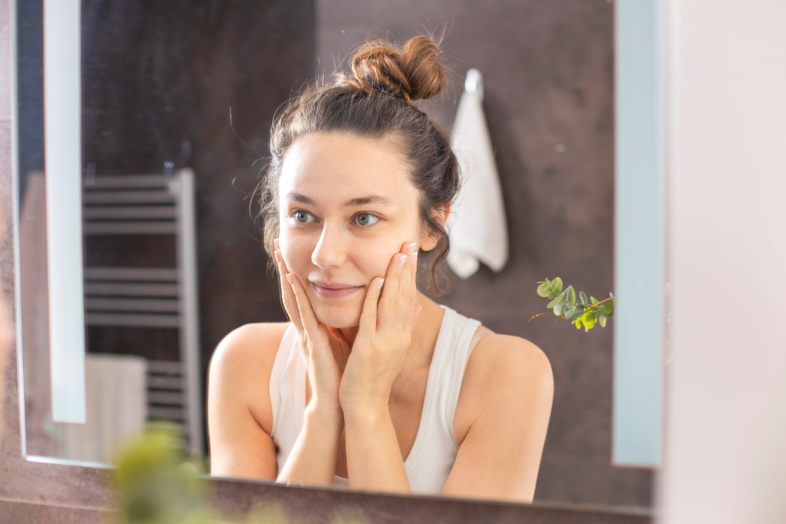 Person touching face while looking at reflection in a bathroom mirror