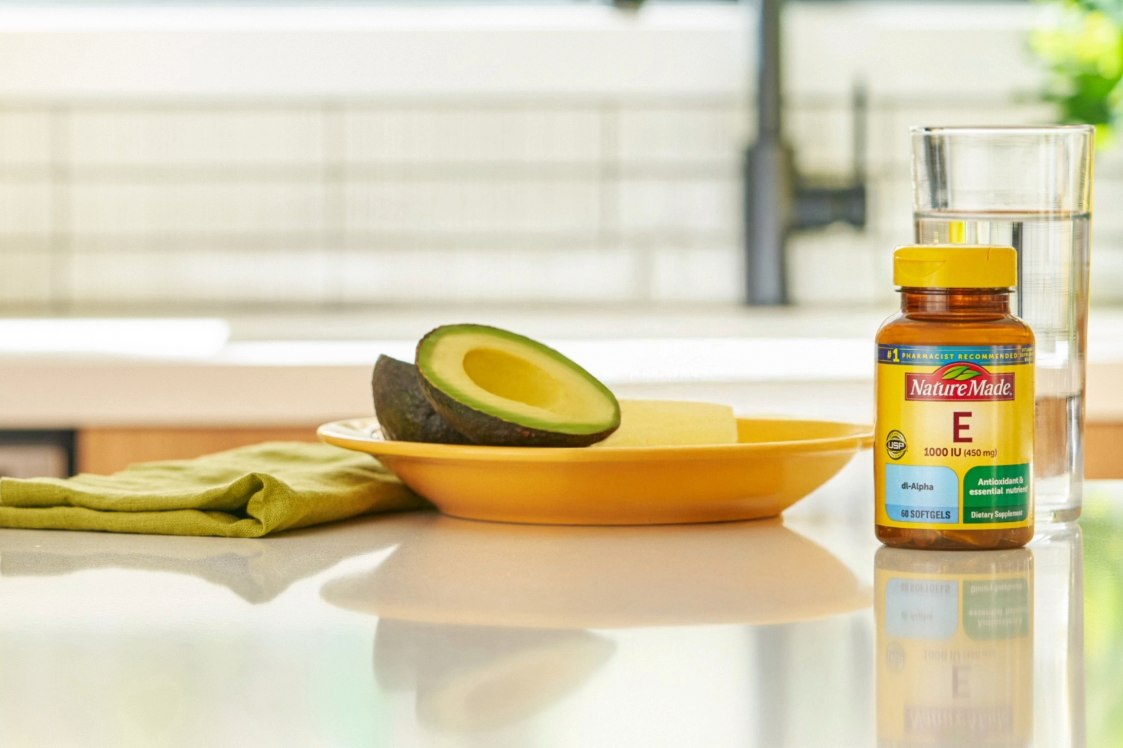 Nature Made Vitamin E bottle with avocado slices and a glass of water