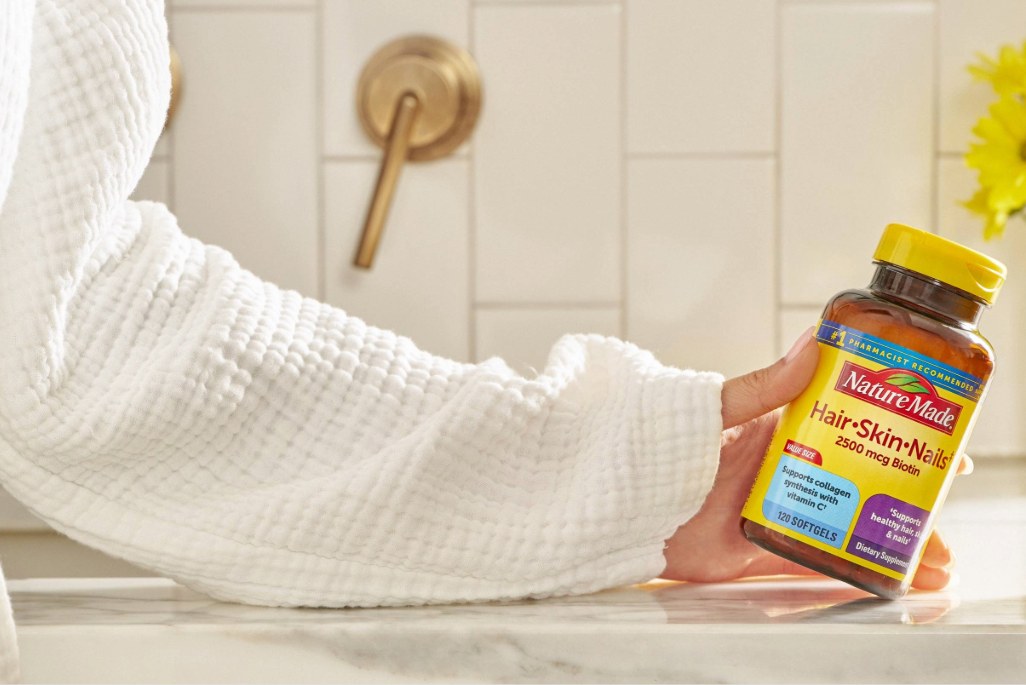 Hand holding Nature Made Hair Skin and Nails supplement bottle on bathroom counter