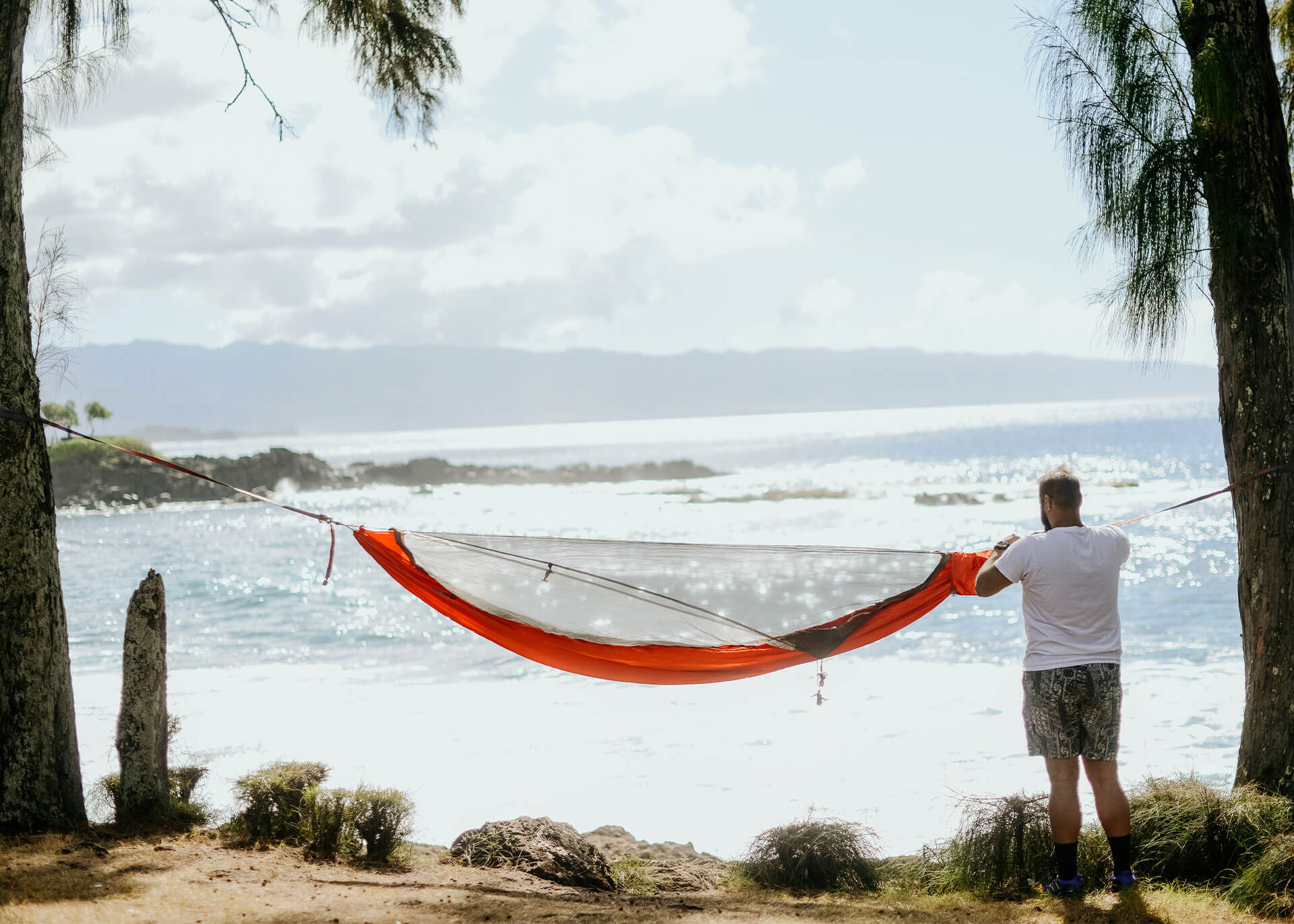 Man setting up a Kammok Mantis all-in-one hammock tent with bug net at the beach for bug protection.
