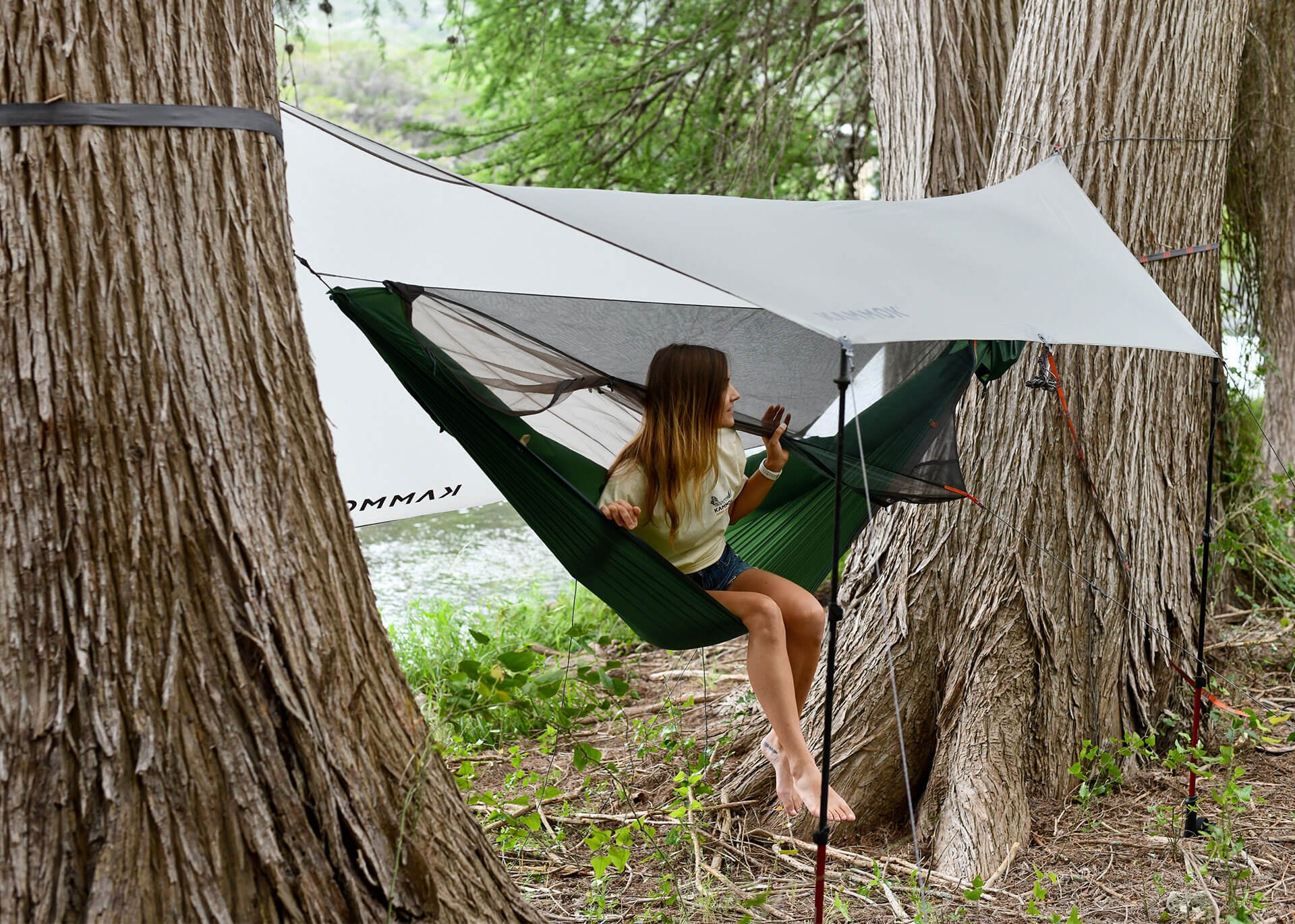 Women sitting in Kammok Mantis all-in-one hammock tent with bug net and weather shelter set up in awning mode.