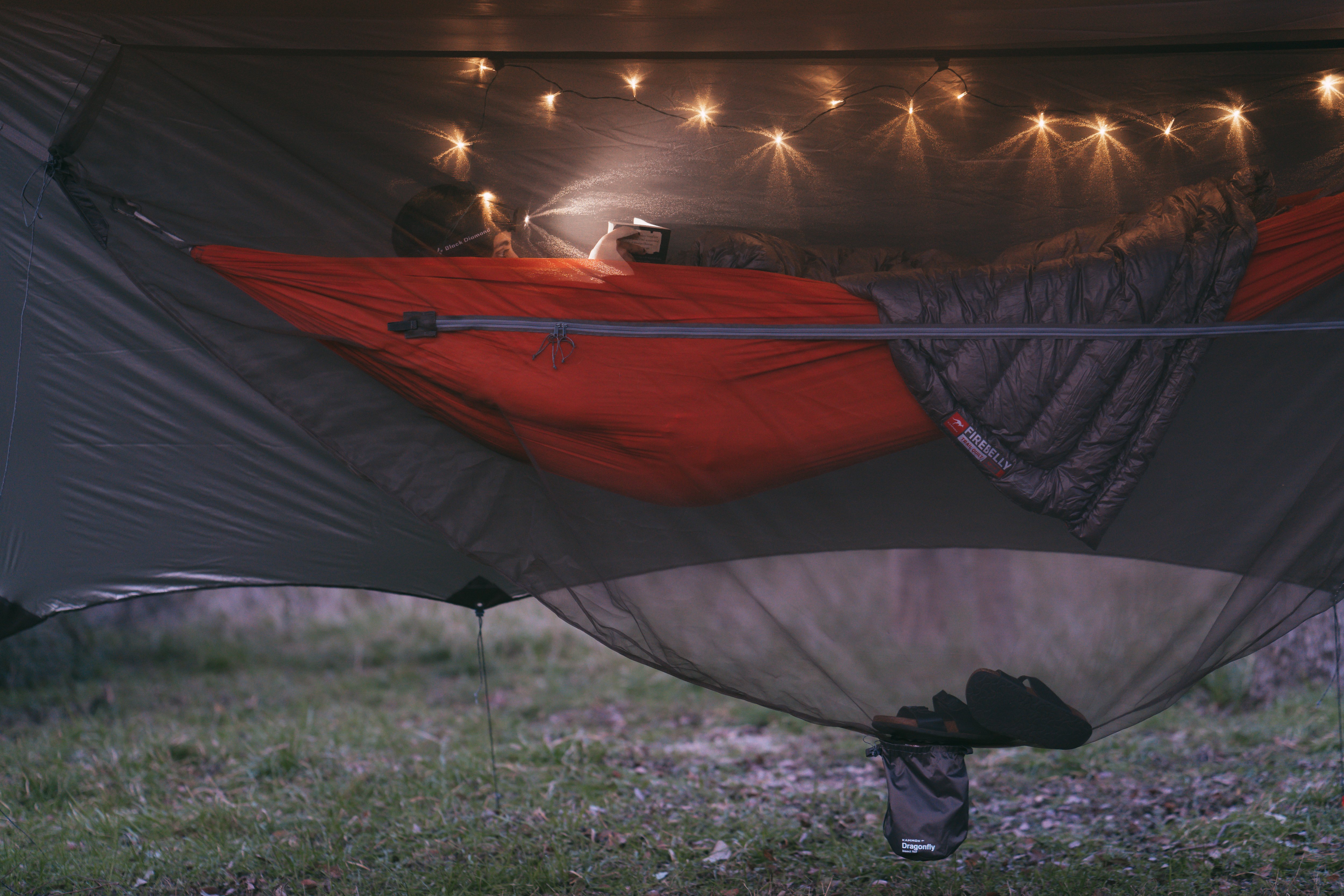 Woman laying in a Roo Double that's surrounded by a Dragonfly Insect Net, with twinkling lights hung above her.