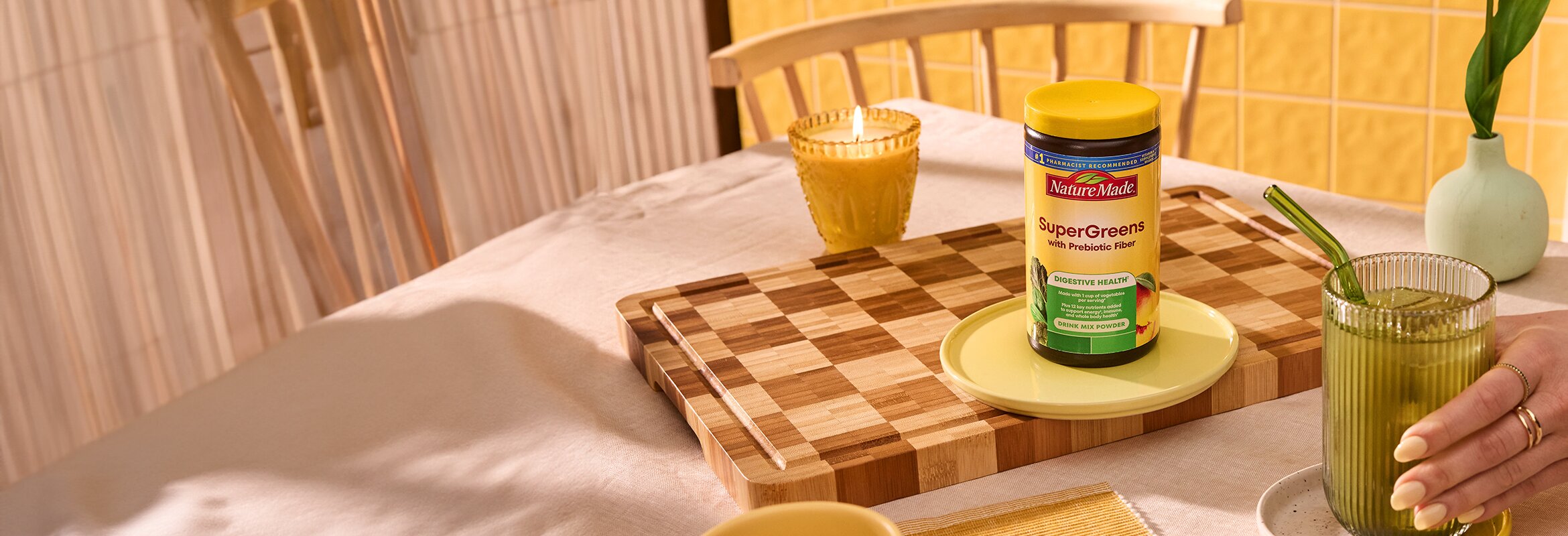 Nature Made SuperGreens with Prebiotic Fiber Mix and a glass of mixed greens on a dining table.