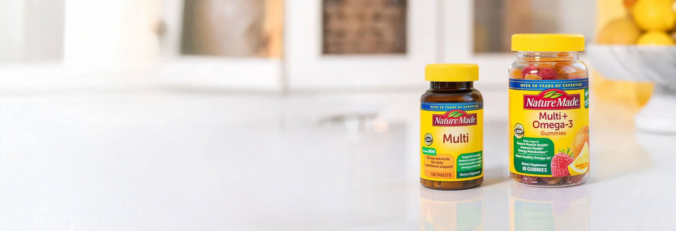 Nature Made Multivitamin tablets and Multi+Omega‑3 gummies displayed on kitchen counter.