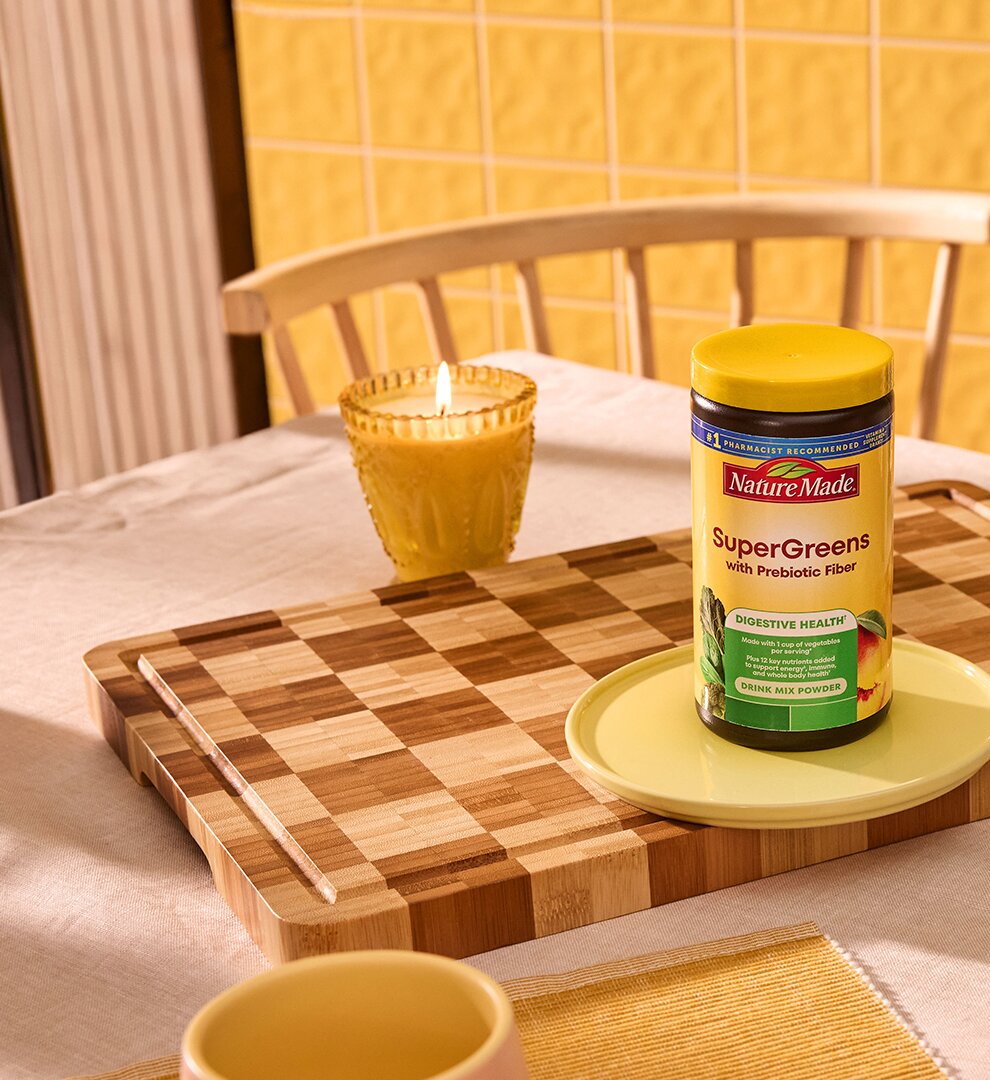 Nature Made SuperGreens with Prebiotic Fiber Mix and a glass of mixed greens on a dining table.