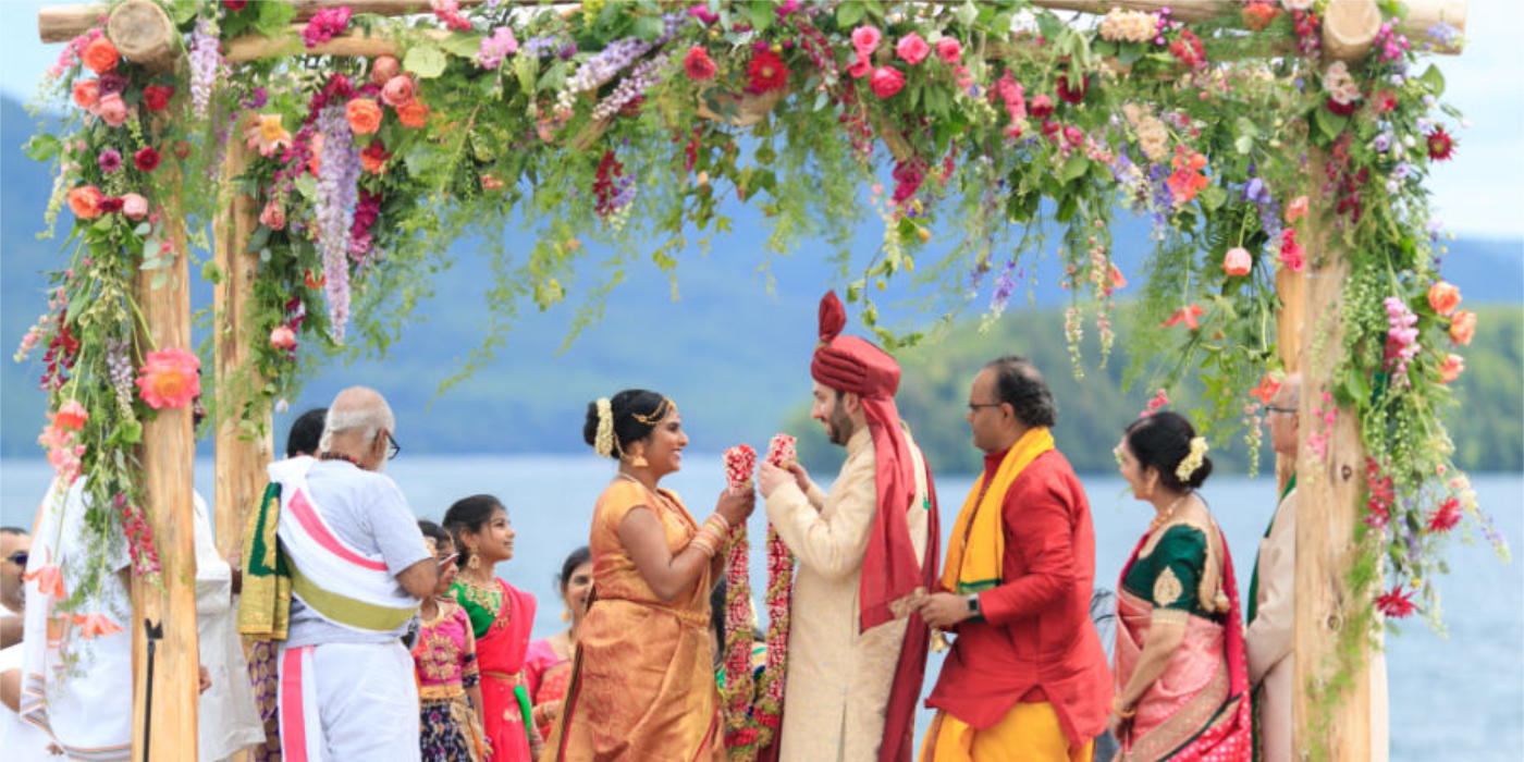 A wedding in front of a lake, a chuppah with vibrant colors flowers and a couple very happy