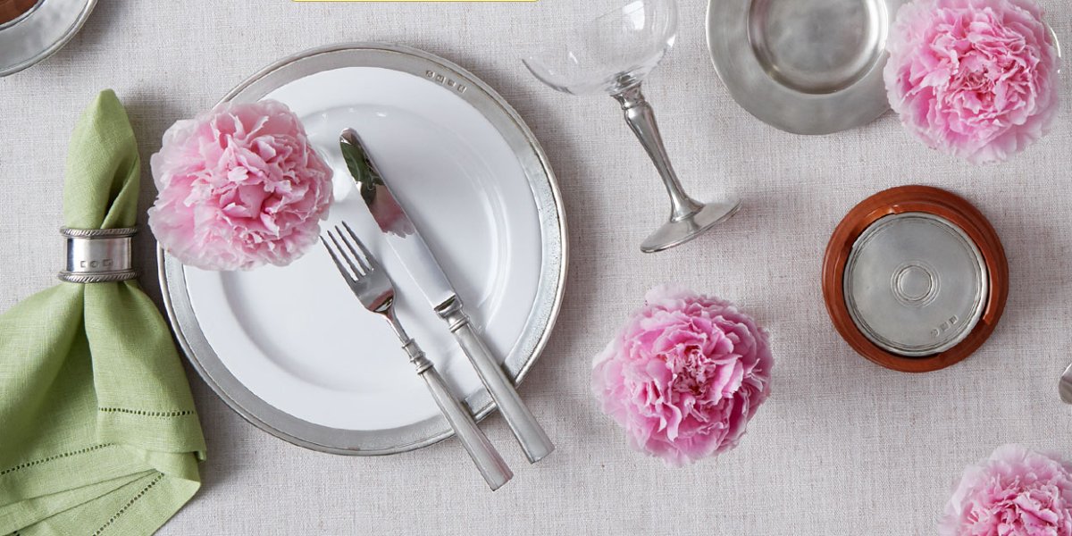 A dinner table with beautiful pewter dinnerware and some flowers decorating the table