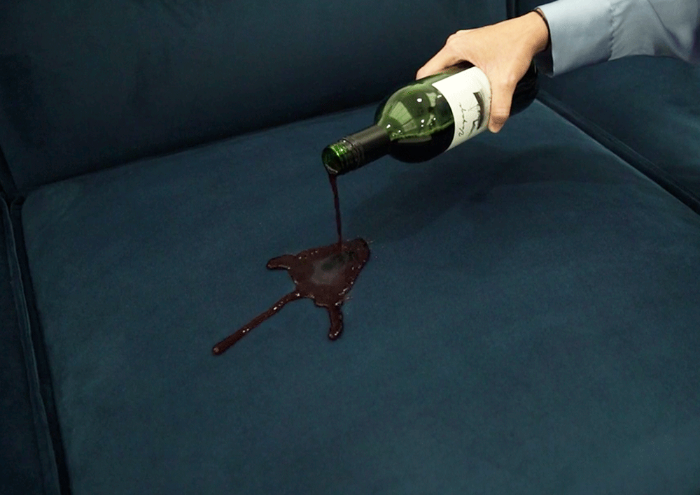 Red Wine being poured onto the seat cushion of teal velvet sofa to demonstrate stain resistance