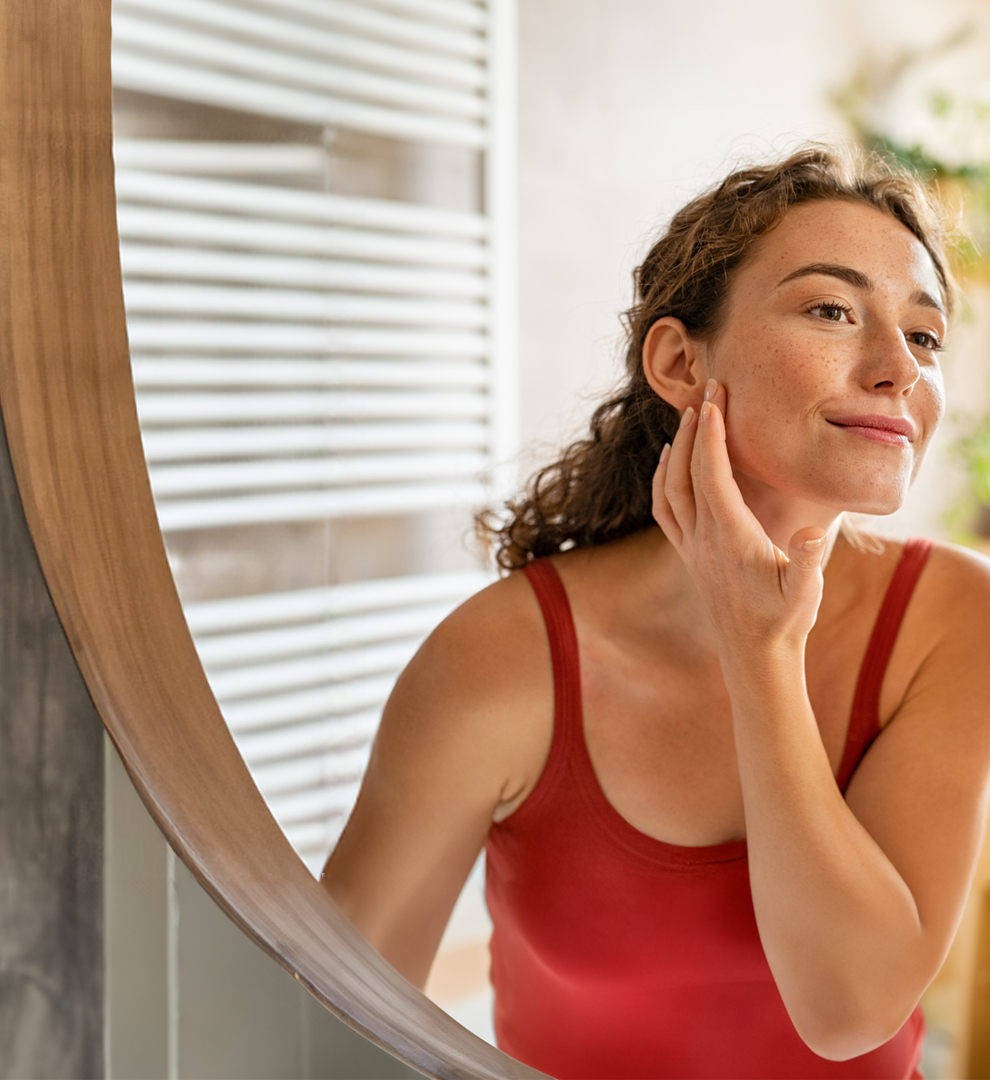 Person in red shirt examining facial skin in mirror at home