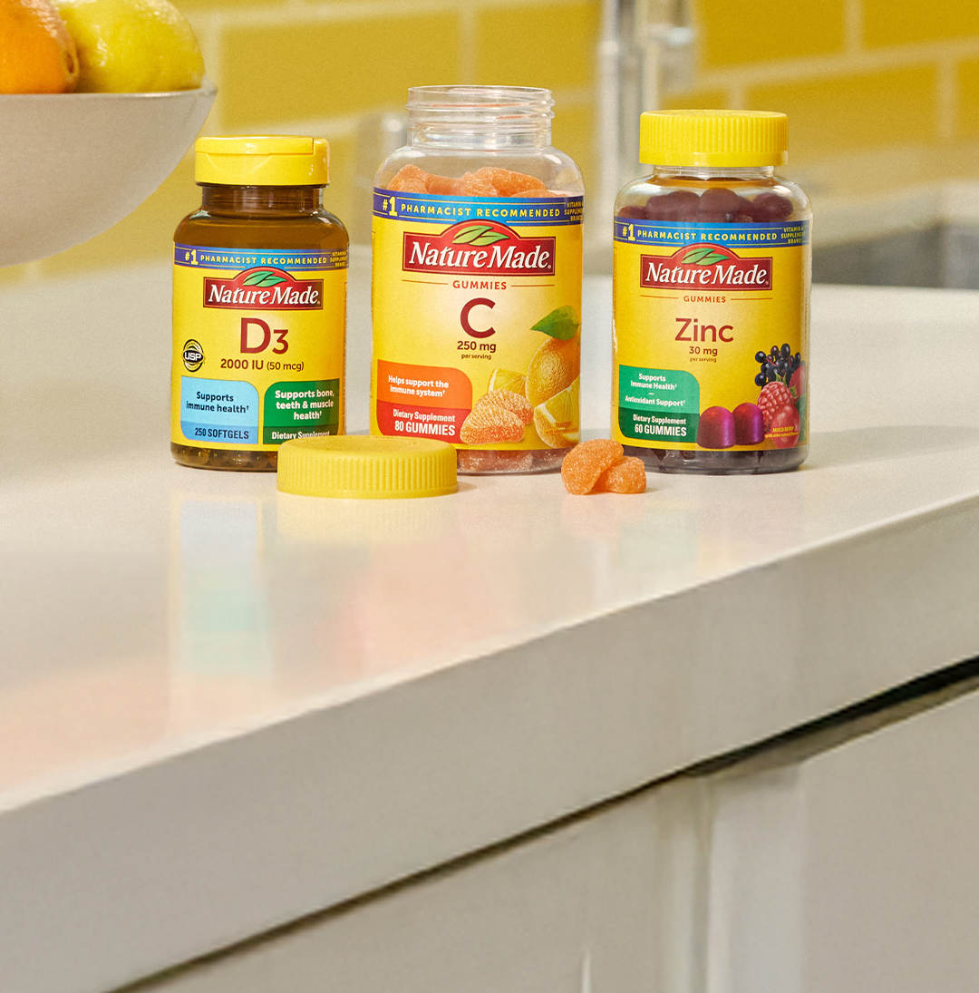 Nature Made Vitamin D3, Vitamin C and Zinc supplements on a kitchen counter top with a bright yellow tile background.