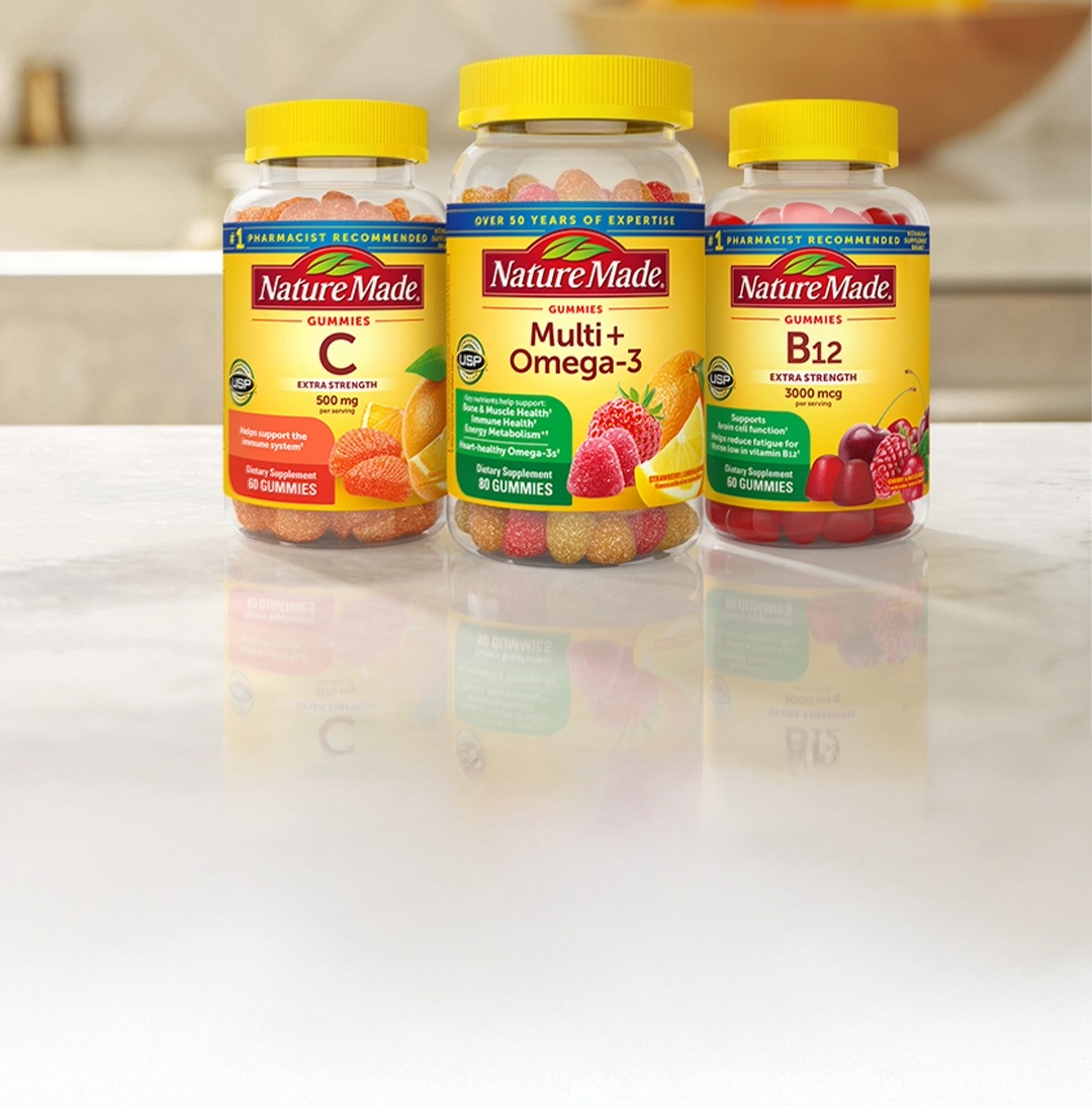 Nature Made gummy vitamins including Vitamin C, Multi+Omega‑3, and B12 bottles on a kitchen counter.