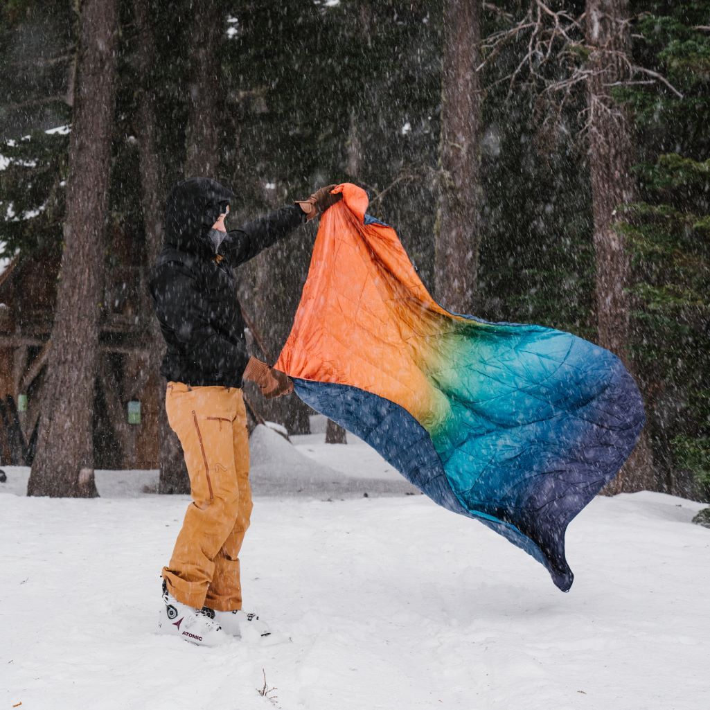 A person whipping out their Rumpl puffy blanket outside while it's snowing
