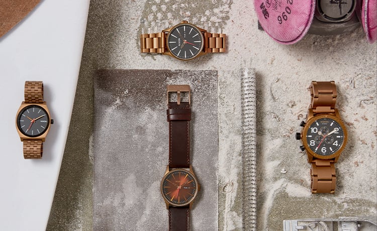 A collection of bronze Nixon watches sit on the surf board getting shaped amongst other common shaping items.