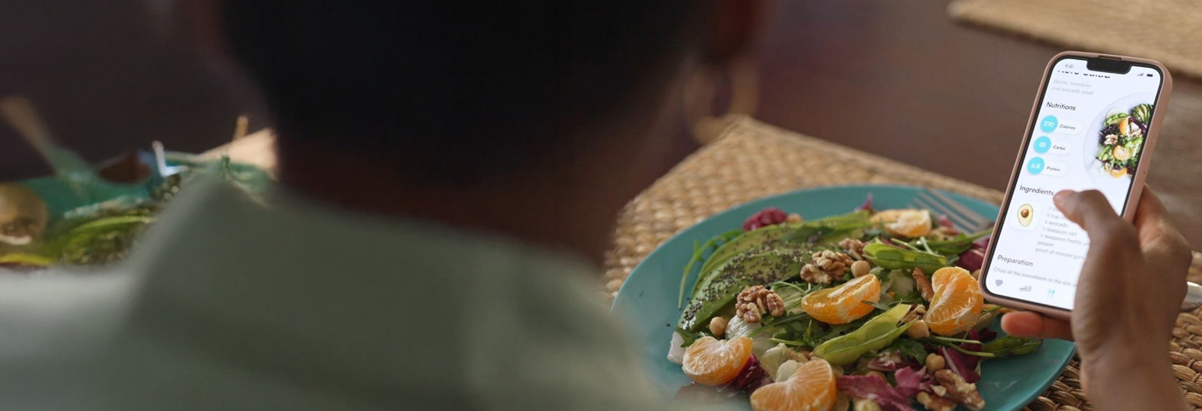 Person viewing a recipe on a smartphone while sitting at a table with a plate of fresh salad.
