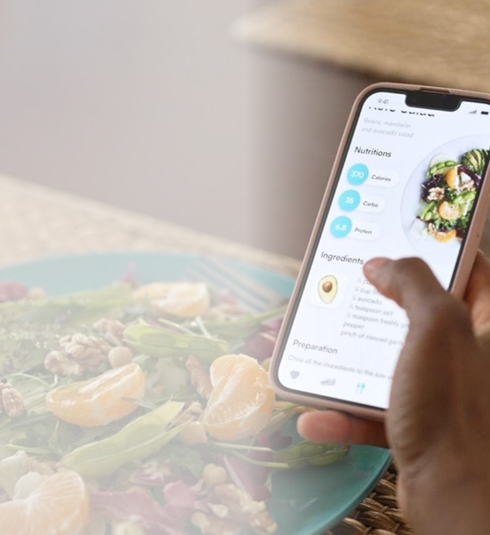 Person viewing a recipe on a smartphone while sitting at a table with a plate of fresh salad.
