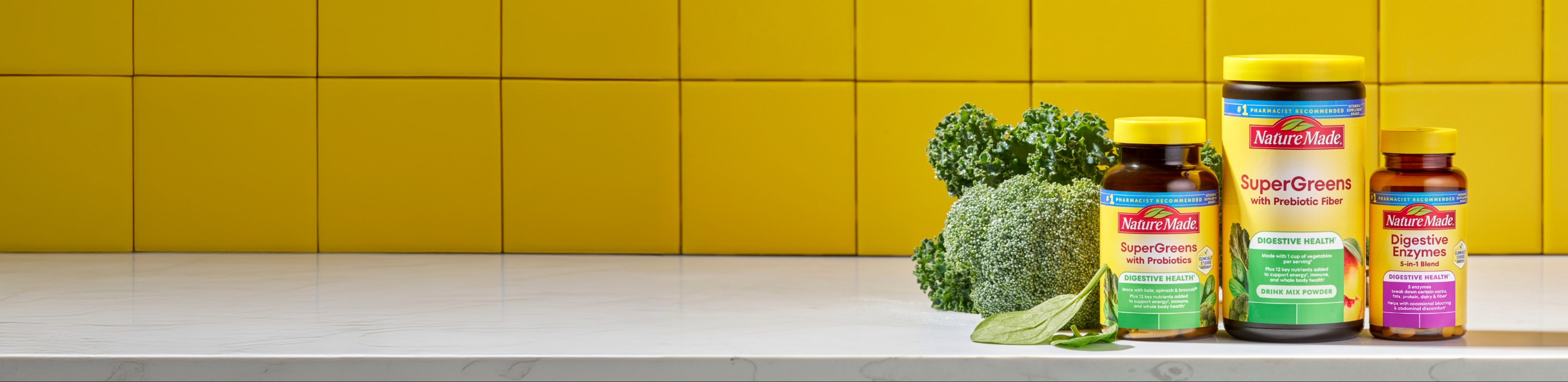 Nature Made SuperGreens and Digestive Enzymes supplements with brocoli and a glass of water on yellow background.