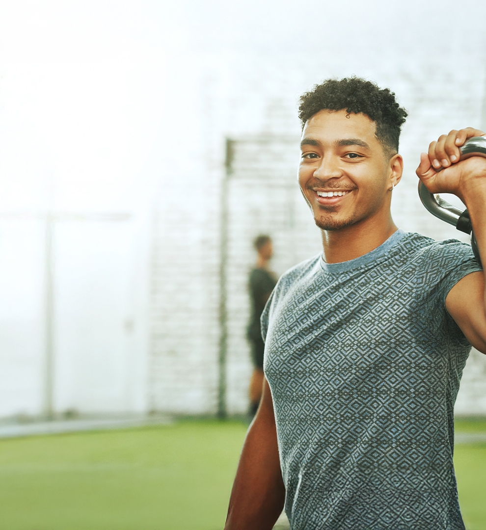 Person performing kettlebell shoulder exercise in a gym with other individuals in the background.