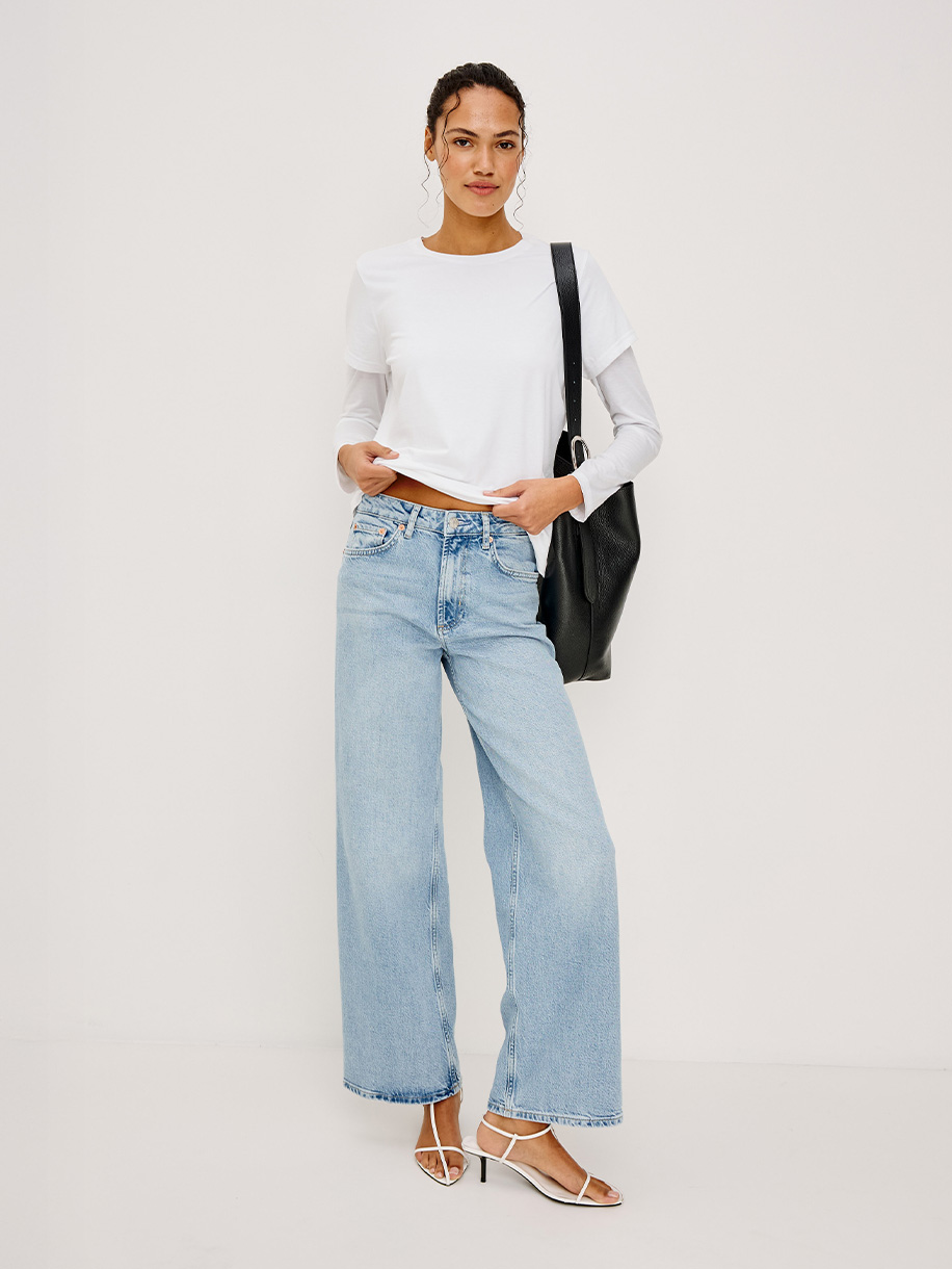 Woman in wide leg jeans on white background. Click here to shop Wide Leg Jeans