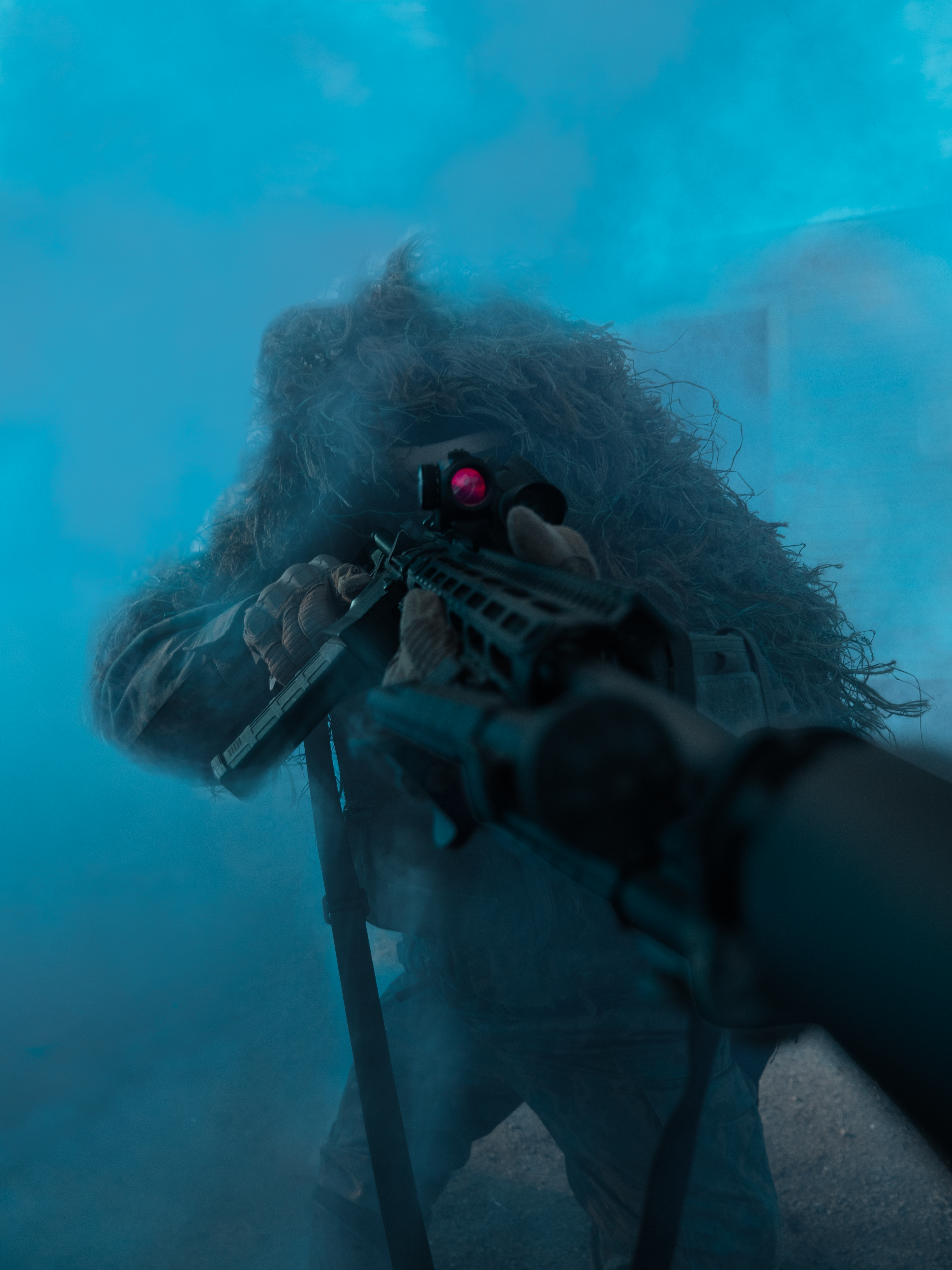 Man standing in blue smoke with a rifle in hand.