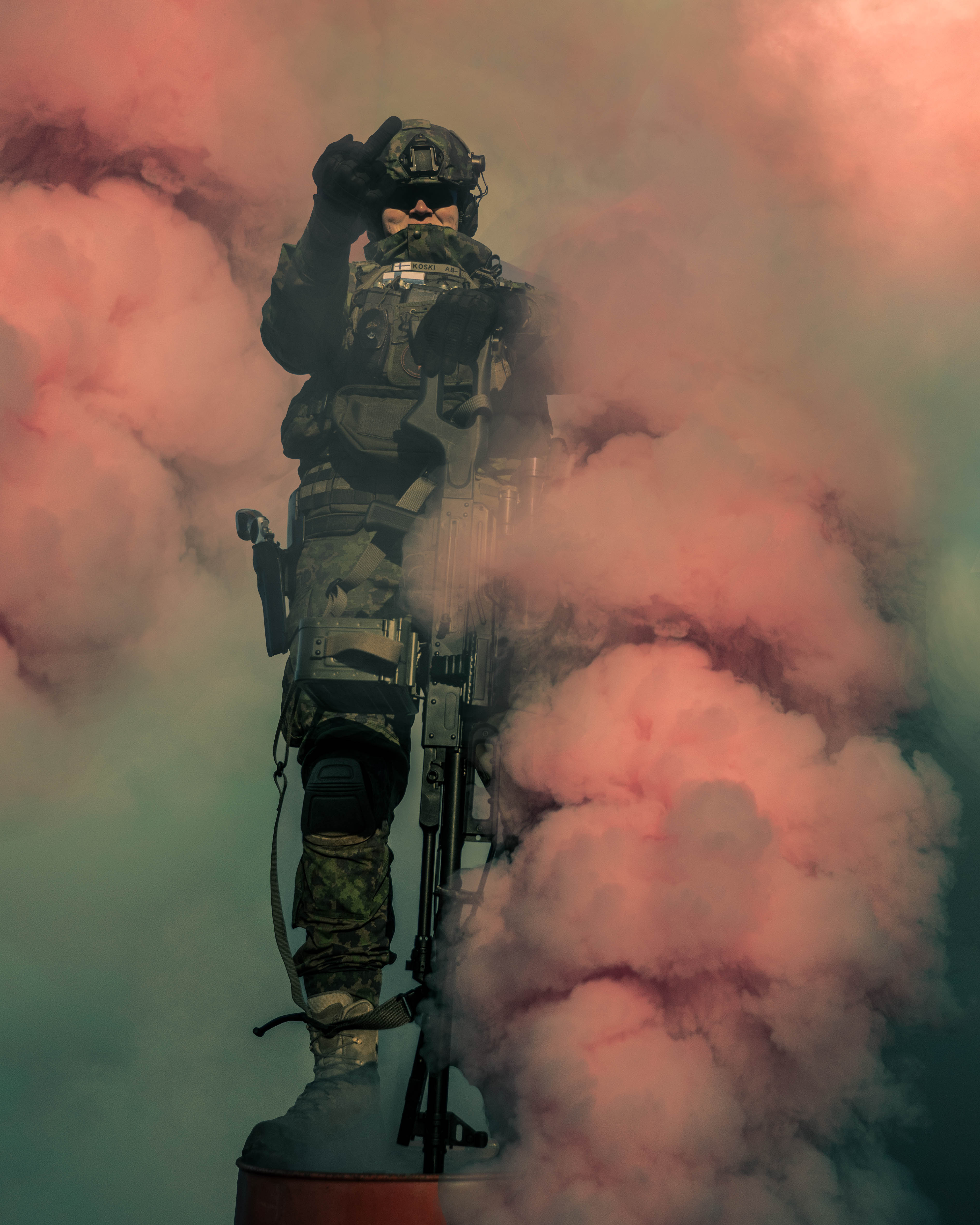 Man standing on a oil barrel in the middle of smoke. He has a light machinegun. 