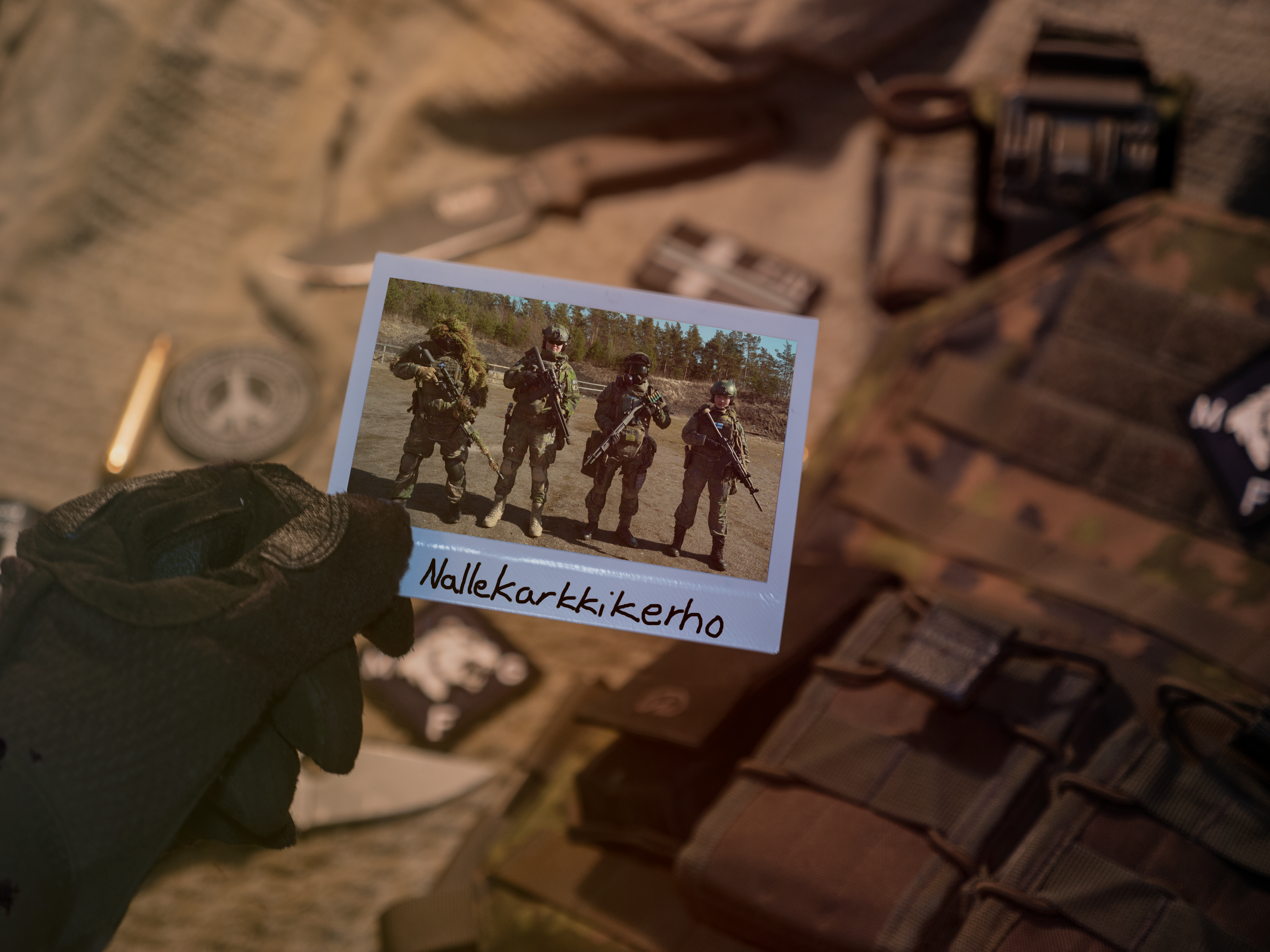 A hand is holding up a polaroid photo of four people in army uniforms.